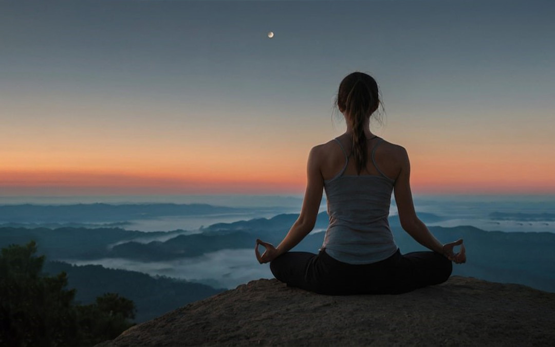 Mujer meditando en la cima de una montaña al entardecer