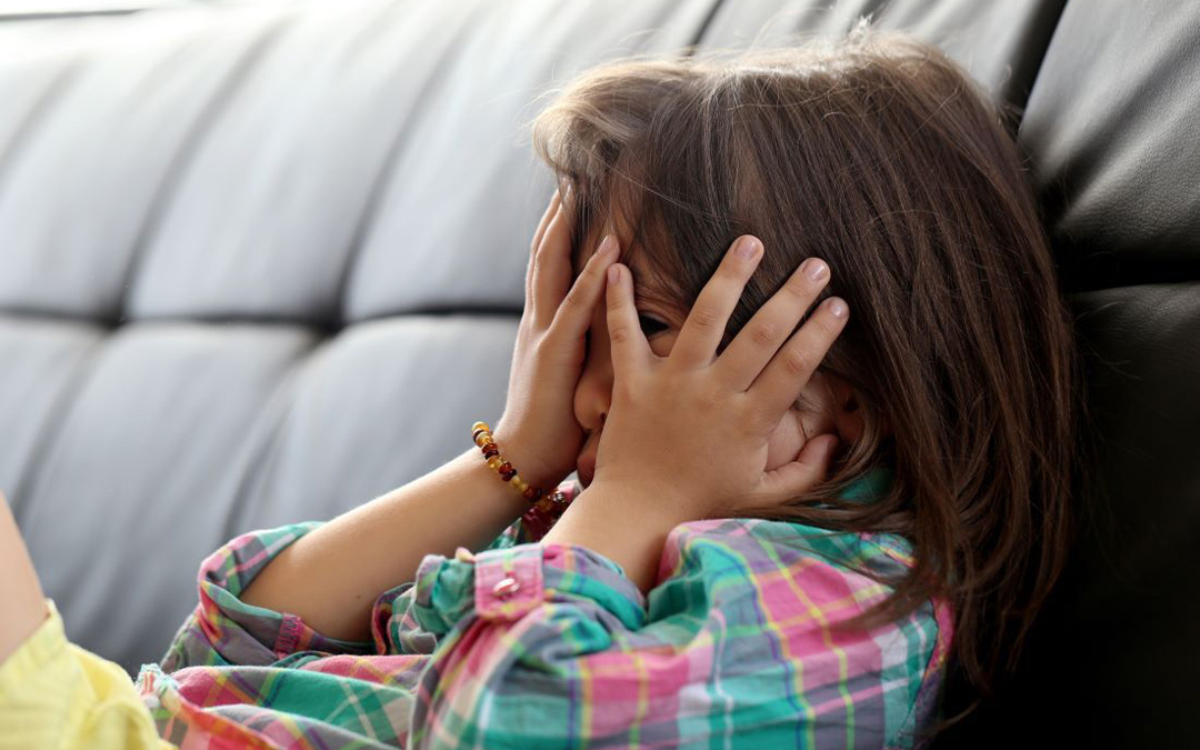 Niño en un sofá con las manos en la cara